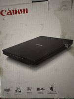 Canon flatbed scanner shown on damaged box with Canon branding and spec icons.