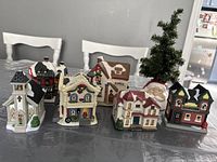 Seven ceramic Christmas village buildings arranged on table with a gray tablecloth in a dining room setting.
