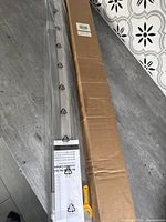 Photo showing the packaging box and the packaged window shade unit with visible manual and adjustment handle.