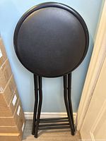 Top view of the black cushioned round seat of the foldable stool.