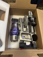 Top view of main vacuum components packed in foam-lined box showing handheld unit, motorized brush head, and possible battery compartment.