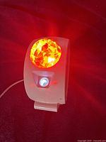 Light projector turned on projecting orange light pattern, showing faceted lens and small clear lens/sensor below it.