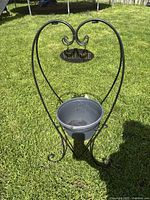 Front photo of black metal heart-shaped planter stand with hanging welcome sign and round planter pot holder.