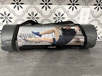 Rolled gray exercise mat with HEAD FITNESS label showing a man exercising, secured with black straps