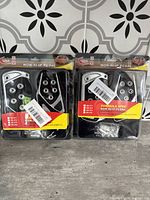 Two new unopened sets of non-slip gas and brake pedal covers in original packaging with mounting hardware visible.