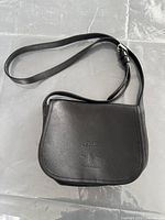 Full view of the black leather purse with adjustable strap laid on a flat surface.