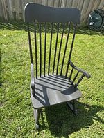 Front angled view of the wooden rocking chair showing spindled backrest, armrests, and seat on grass.