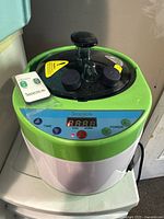 Front view of the SereneLife green and white portable sauna steam machine with remote on top, showing digital display and controls