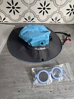 Blue and black wide brim toddler sun hat with ventilation and adjustable chin strap, lying flat on surface.