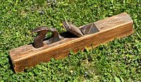Photo of the antique wooden hand plane tool placed on grass, showing the length, hand grip handle, and metal blade.