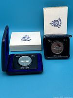 View of two 1973 Canada PEI commemorative nickel dollar coins in blue velvet-lined clamshell cases with original Canada-branded cardboard sleeves, shown side by side.