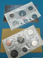 Photo showing two sealed Canadian coin sets in original cellophane packs placed on their certificates and envelopes.