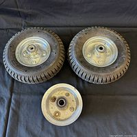 Pair of utility cart tires with metal hubs and one extra metal hub shown on a black cloth background.