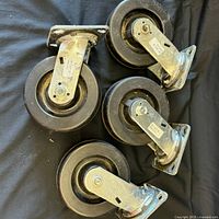 Top view of all four black caster wheels arranged on a black surface showing metal swivel brackets and mounting plates.