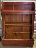 Front view of antique wooden wall shelf showing three compartments: two shelves and a large bottom compartment. The shelf is reddish-brown on the outside and natural wood color inside.