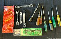 Overall top view of ratchet wrenches, screwdrivers, and safety glasses on black background