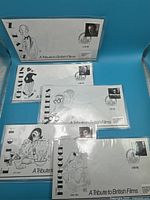 Five First Day Covers arranged on blue background, each with different British actors drawn in sketch form and with respective postage stamps.