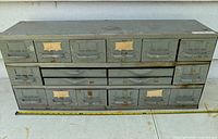 Front view of steel cabinet showing multiple drawers with label holders and metal handles, and a tape measure placed for scale.
