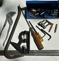Wide view photo of assorted hand tools including pliers, pry bar, combo square, screwdrivers, hex keys, and various sockets and bits spread out on white surface.