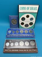Four coin sets displayed: 1967 Jerusalem Specimen Set, 1973 and 1974 Official Mint Sets and commemorative coin in package.