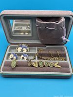 View of pansy enamel brooch, matching stud earrings, and fish stone pendant necklace inside velvet-lined travel box with mirror and pouch