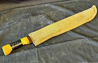 Closed view of ZIP brand garden machete inside beige fabric sheath showing wrapped handle