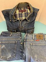 Three denim pieces shown folded on flat surface: Levi's jeans, Wrangler jeans, and Nevada denim jacket with collar and lining visible.