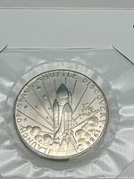 Image showing the silver-tone commemorative coin featuring the Space Shuttle Discovery launch design, dated 1988, with denomination $5.