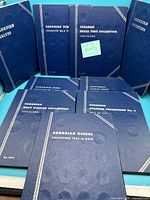 Lot of nine blue Whitman Canadian coin holder books displayed showing front covers with embossed silver titles and decorative borders.