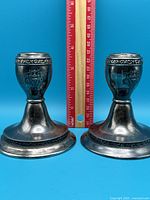 Pair of nearly 4 inch high metal candlesticks with dark patina and crest on sides. Ruler included for scale.