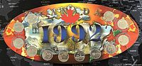 Photo of the oval display board with 12 nickel plated steel Canadian 25 cent coins from 1992 arranged around the perimeter, each representing a province or territory with respective provincial designs.