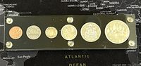 Six Canadian coins displayed in a black acrylic holder with gold screws, showing reverse coin designs including coat of arms and traditional Canadian imagery.