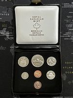 Top view of the case holding the 7 Canadian coins arranged in two rows inside a black velvet interior with white lid featuring Royal Canadian Mint logo.