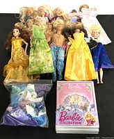 Multiple Barbie dolls and one Ken doll laid out, with assorted clothing items and Barbie Island Princess DVD in view.