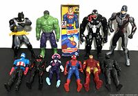 Group photo showing all 11 superhero action figures arranged in two rows on a black surface with a white background.