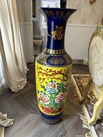 Front angle view of tallest portion of vase showing yellow base with colorful detailed flowers and blue neck with gold Chinese characters.