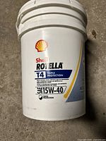 Front view of white plastic 5 gallon pail labeled Shell Rotella T4 Triple Protection SAE 15W-40 oil.