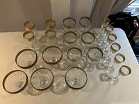 Top and angled view of tall stemmed crystal glasses with plain gold rims arranged on a table.