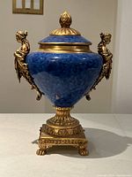 Front view of blue and gold urn with figural handles on table