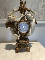 Close-up of the gold cherub decorative clock, showing two cherubs holding the clock and intricate gold detailing.