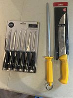Large yellow-handled chef's knife with matching sharpening steel rod beside it, blade visible in packaging for knife, steel rod unboxed.