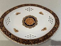 Top angled view of white porcelain dish with gold ornate rim, central medallion and lattice cutouts