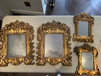 Top-down view of four decorative mirrors with ornate gold frames laid on a table, showing overall shape and size differences.
