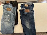Four pairs of ladies jeans folded and stacked, showing various washes and leather patch logos.