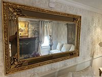Front view of gold ornate rectangular wall mirror mounted on patterned wallpaper