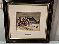 Framed artwork showing entire piece including mat and plaque, capturing the winter village scene with snow, houses, and road.