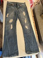 Full length front view of jeans showing distressed areas on legs and boot cut style.