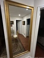 Full length rectangular mirror mounted on wall reflecting hallway and doorways.