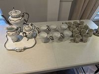 Full view of all items displayed on table showing the teapot, creamer, sugar bowl on tray, 6 larger tea cups, and 8 smaller espresso cups arranged separately.