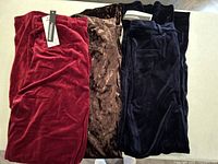 Three pairs of velvet pants in red, brown, and dark blue stacked together showing soft velvet texture and tags.